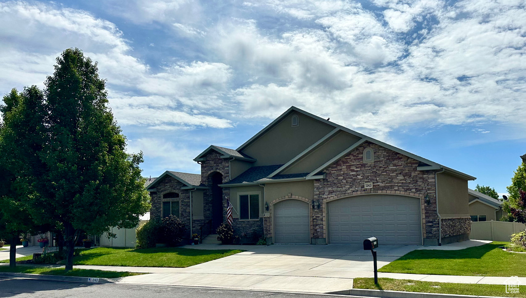 View of front of house with stucco siding, driveway, an attached garage, and stone siding
