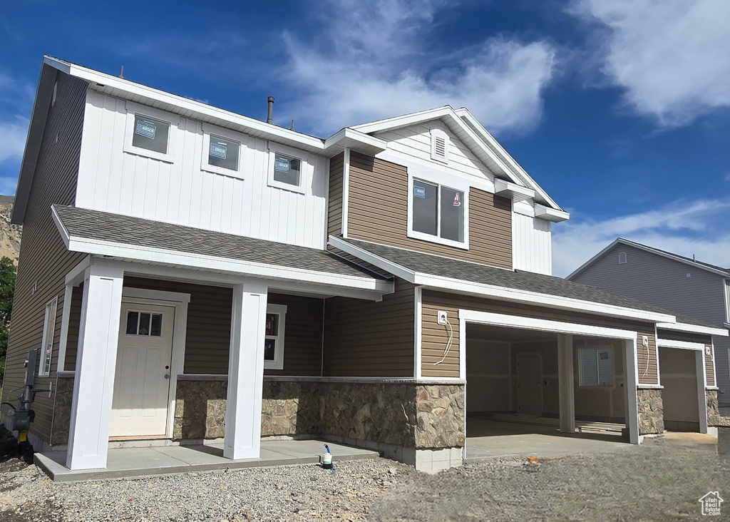 View of front of house with stone siding, covered porch, board and batten siding, and an attached garage