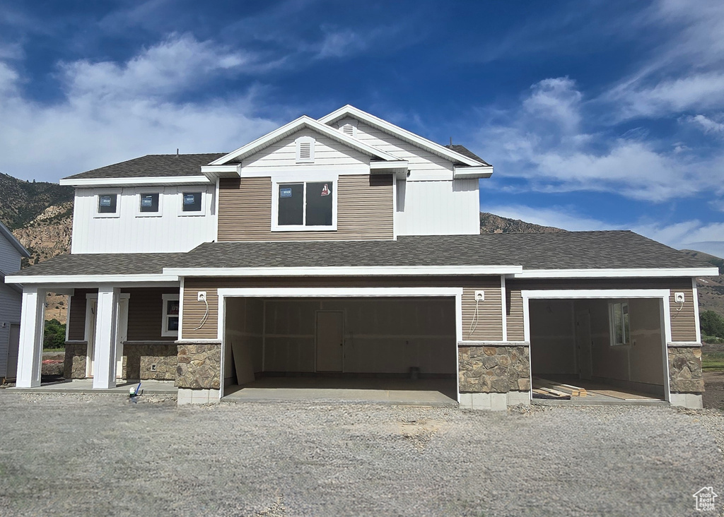 View of front facade featuring stone siding, gravel driveway, roof with shingles, and a porch