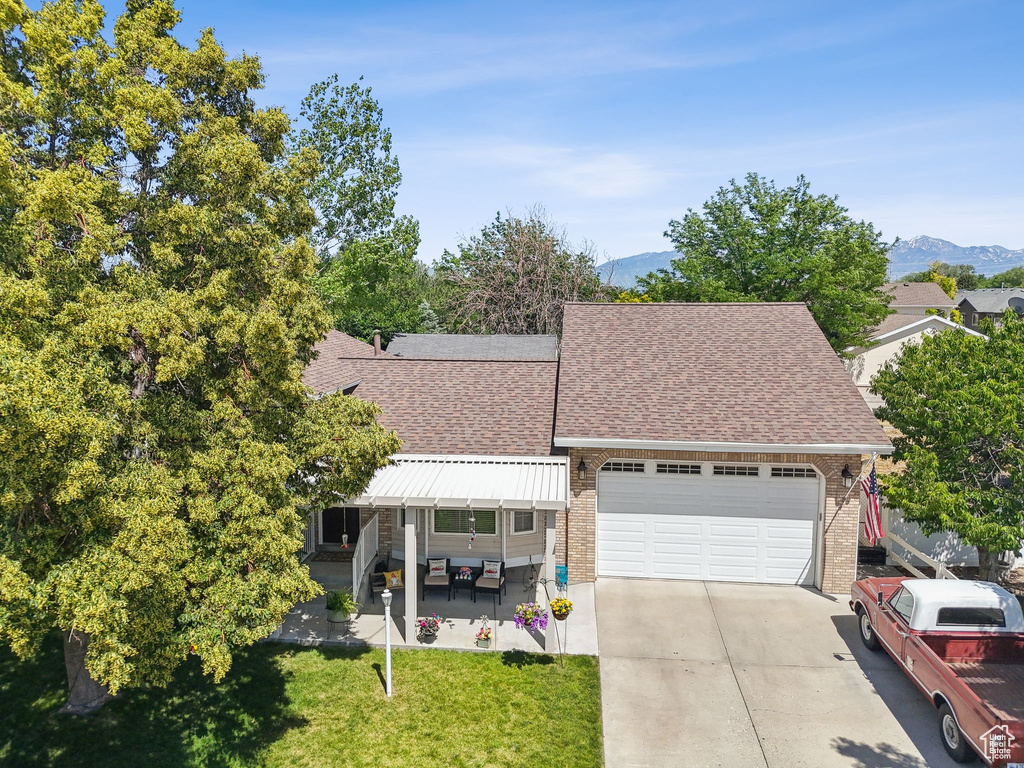 View of front of home with roof with shingles, an attached garage, driveway, a mountain view, and a front lawn