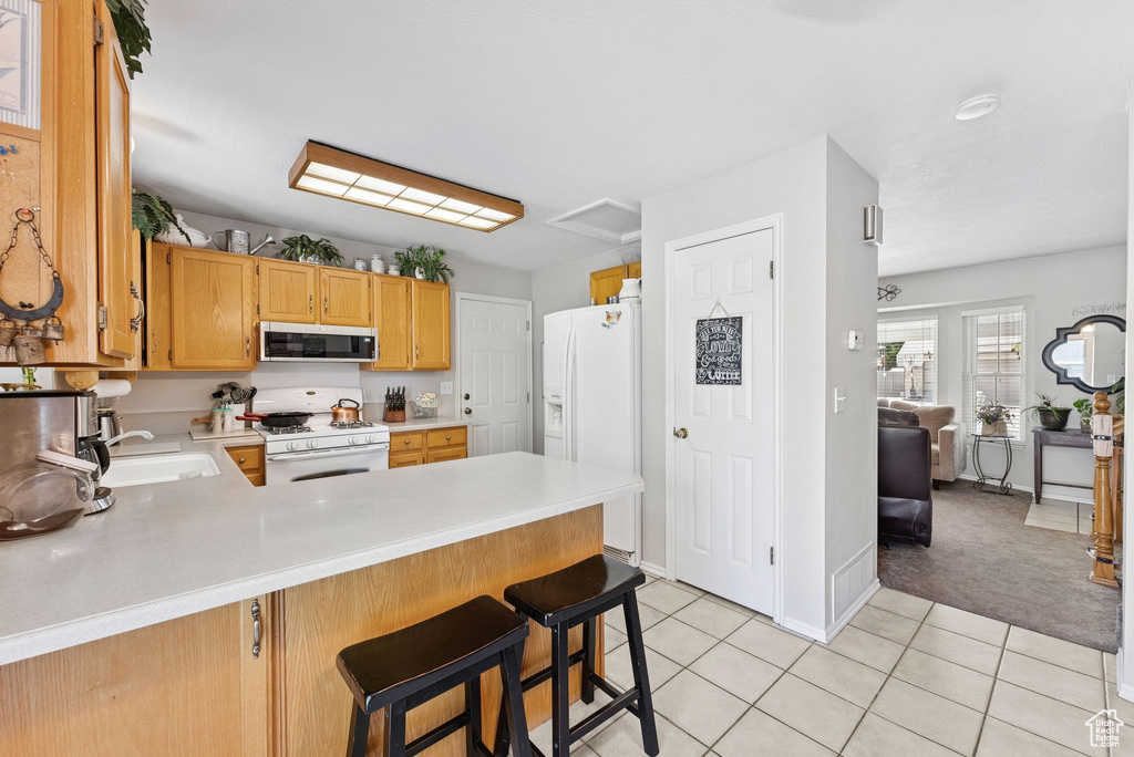 Kitchen with white appliances, light countertops, light tile patterned flooring, a peninsula, and light colored carpet