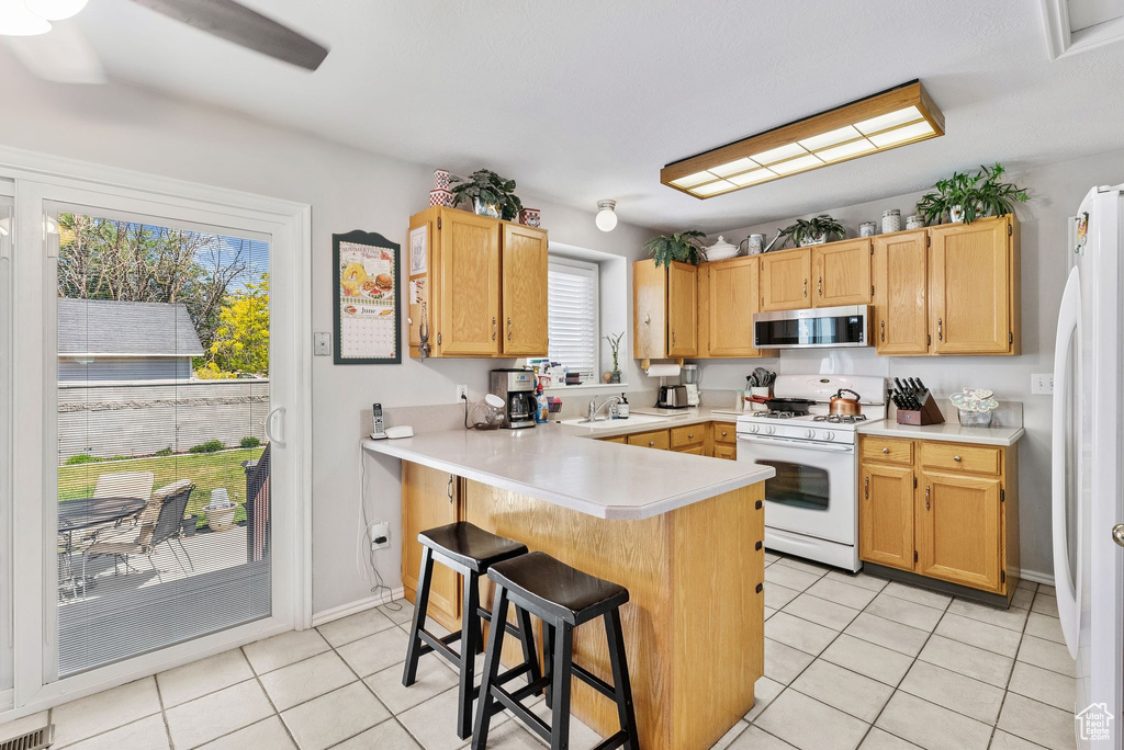 Kitchen with white appliances, light tile patterned floors, a peninsula, a breakfast bar area, and light countertops