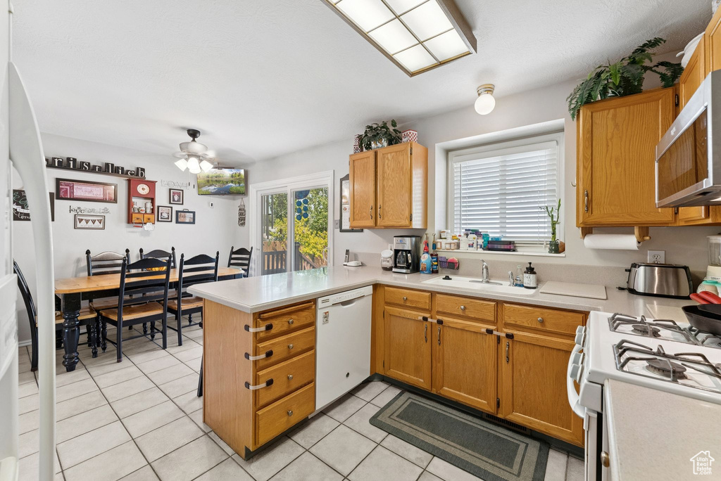 Kitchen with white appliances, a peninsula, light countertops, and light tile patterned flooring