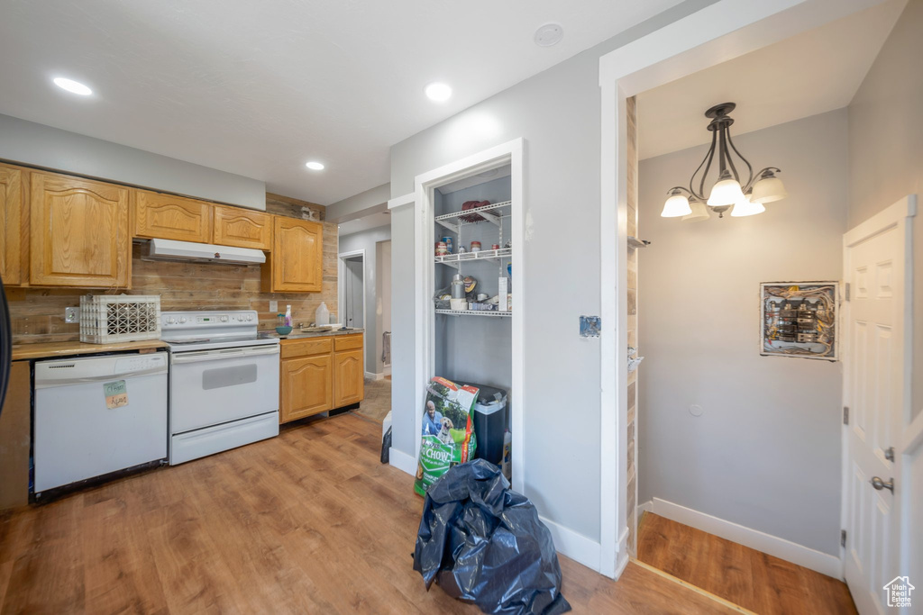 Kitchen featuring white appliances, under cabinet range hood, tasteful backsplash, light countertops, and light wood finished floors