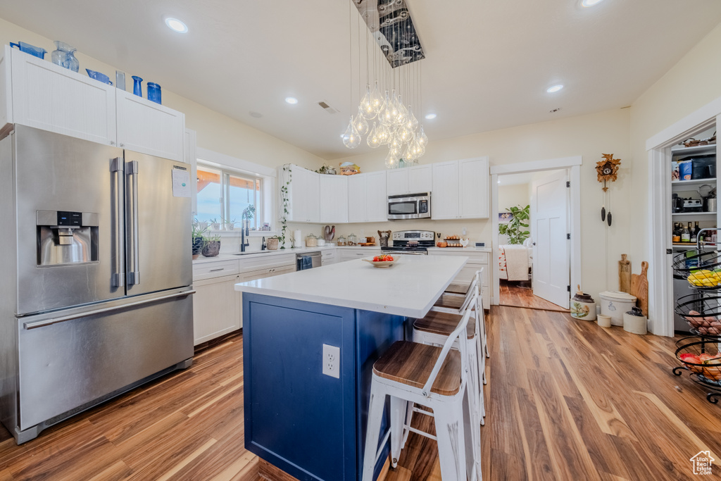 Kitchen featuring stainless steel appliances, light wood-type flooring, a kitchen island, white cabinetry, and recessed lighting