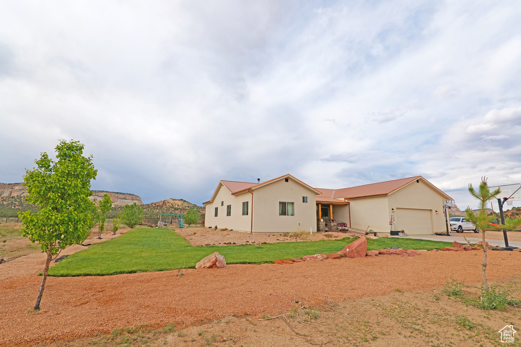 Back of property featuring an attached garage, concrete driveway, stucco siding, and a yard