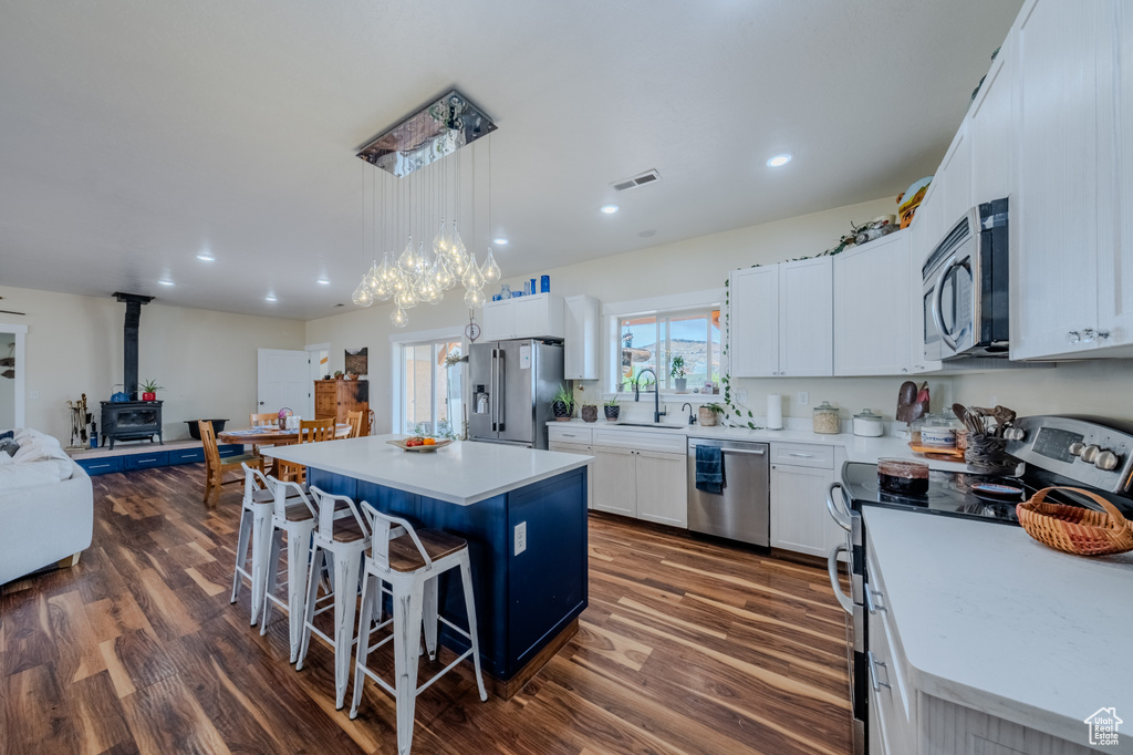 Kitchen featuring stainless steel appliances, a wood stove, a kitchen bar, a kitchen island, and dark wood-style floors