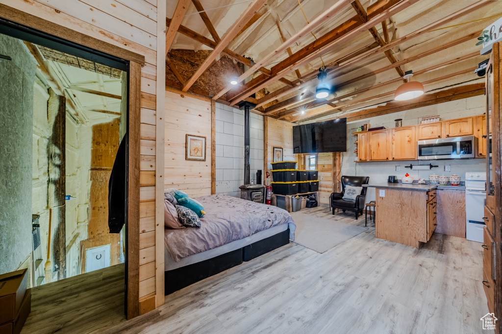Bedroom featuring wooden walls, light wood-style floors, and a wood stove