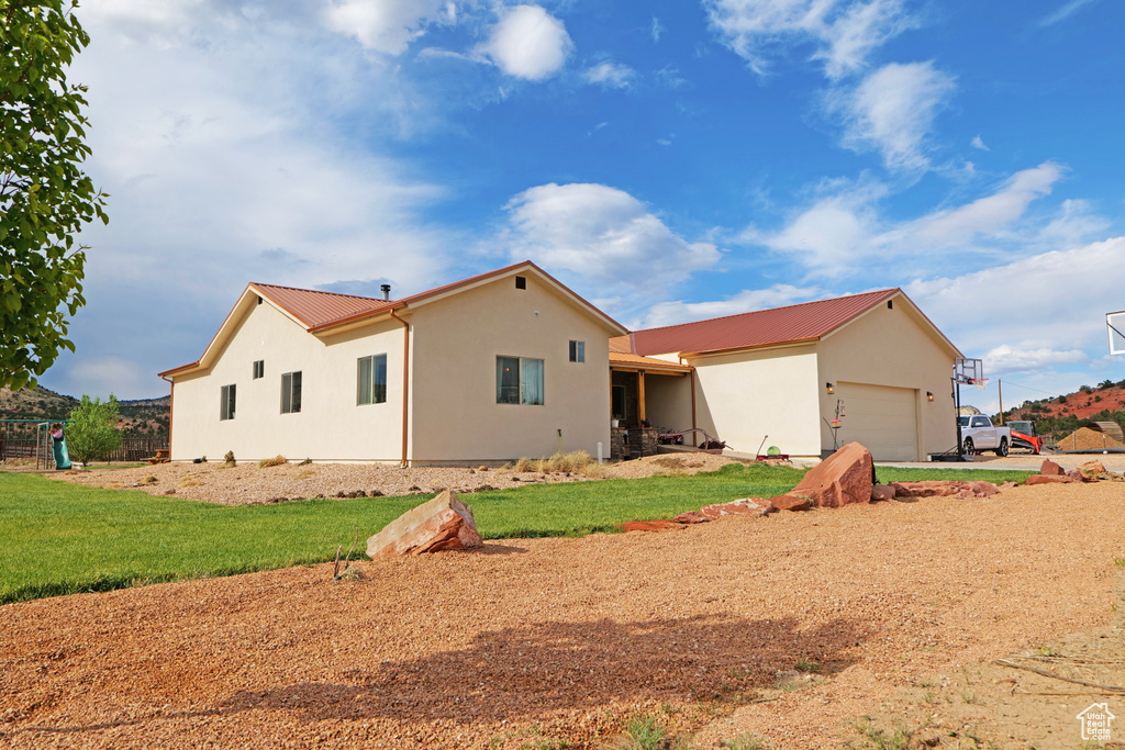 Rear view of house featuring stucco siding, a metal roof, a garage, and a lawn