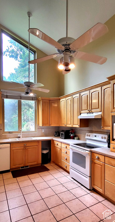 Kitchen with white appliances, high vaulted ceiling, under cabinet range hood, a ceiling fan, and light tile patterned floors