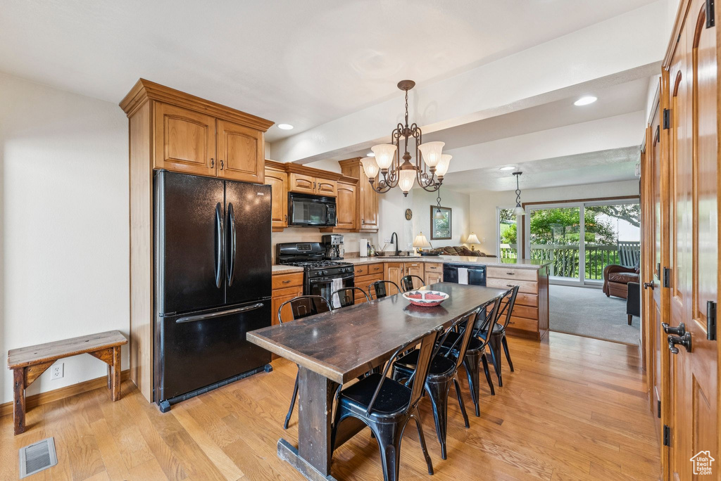 Kitchen with black appliances, a peninsula, light wood-style flooring, a chandelier, and decorative light fixtures