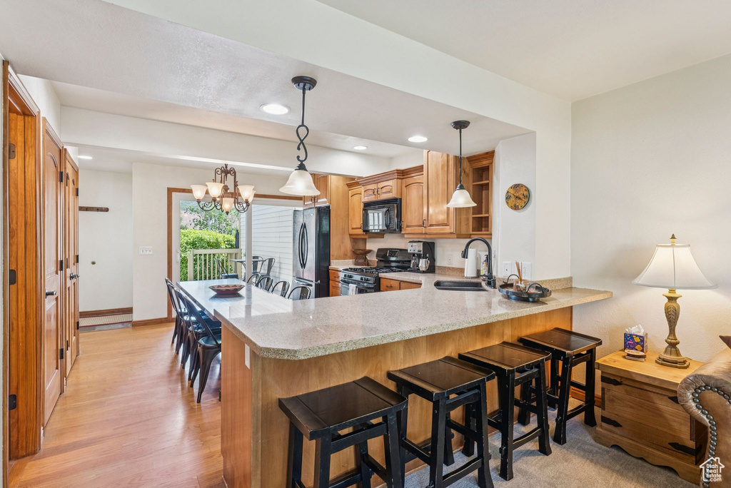 Kitchen featuring black microwave, gas range, freestanding refrigerator, a peninsula, and a breakfast bar