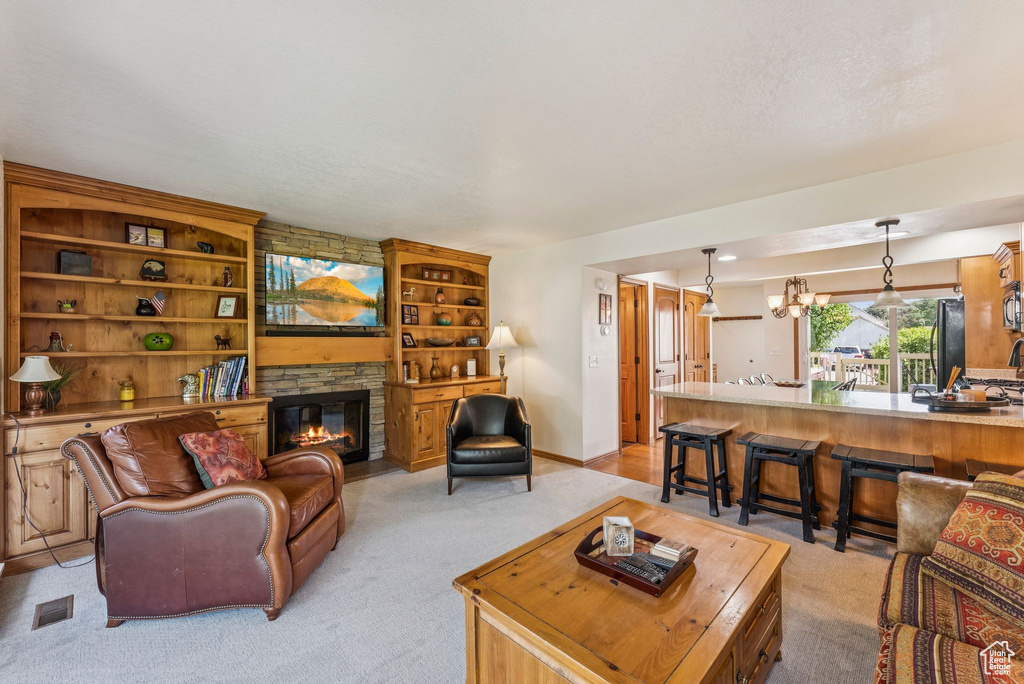 Living room featuring light colored carpet, a stone fireplace, and a chandelier