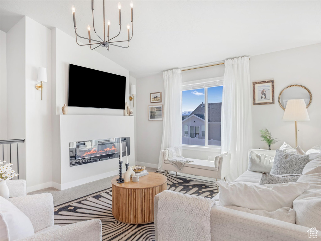 Living area with a chandelier, vaulted ceiling, a glass covered fireplace, carpet, and baseboards