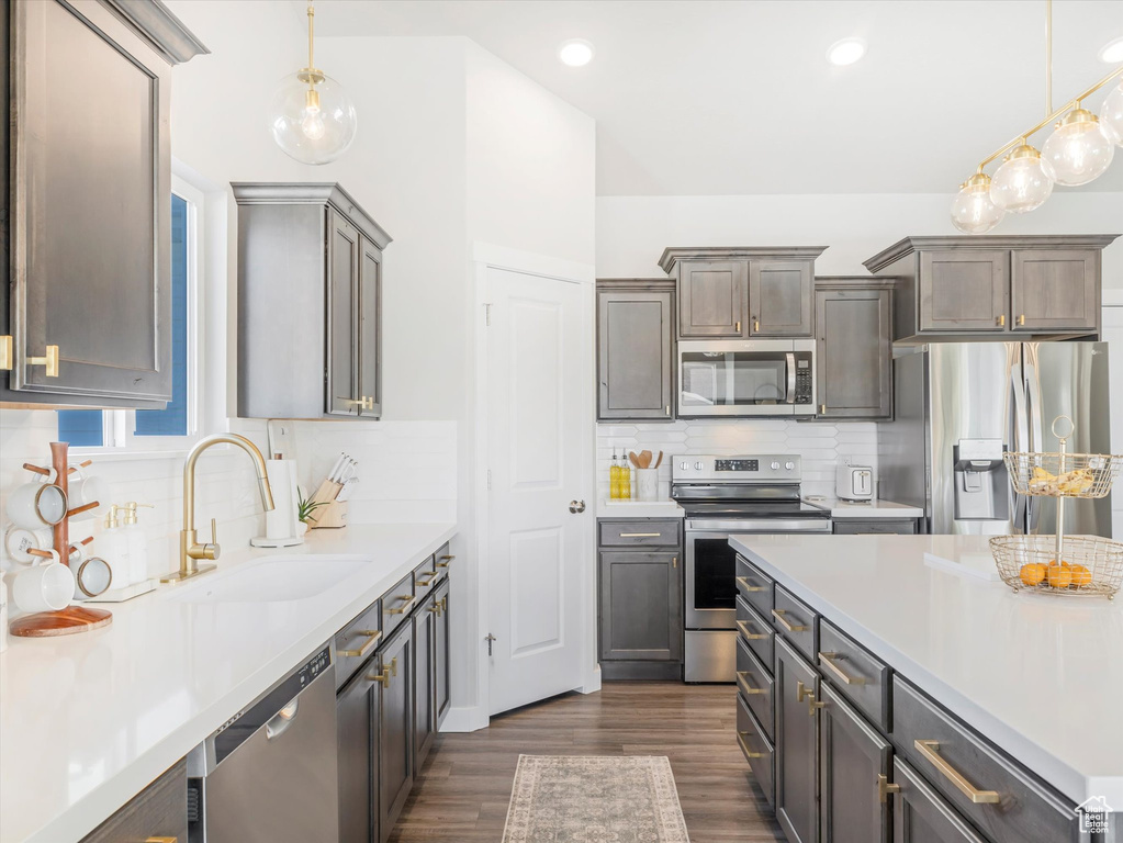 Kitchen featuring stainless steel appliances, a sink, light countertops, decorative backsplash, and decorative light fixtures