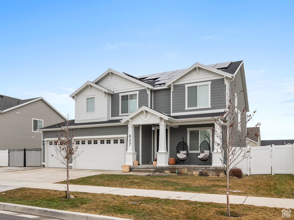 Craftsman-style house featuring covered porch, an attached garage, solar panels, driveway, and a gate
