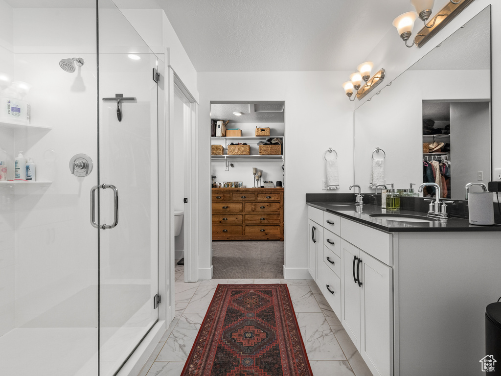 Full bath featuring marble finish flooring, double vanity, a stall shower, and a spacious closet