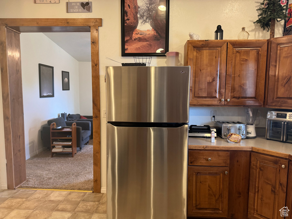 Kitchen featuring freestanding refrigerator, light countertops, lofted ceiling, and light carpet