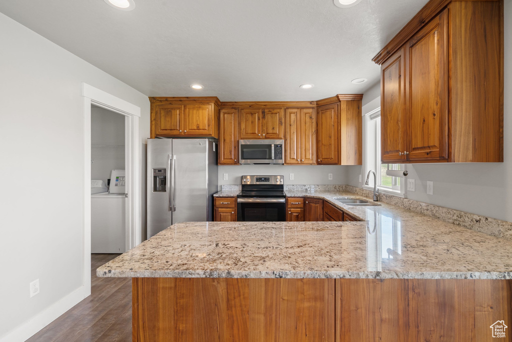 Kitchen with appliances with stainless steel finishes, brown cabinetry, a peninsula, recessed lighting, and dark wood-type flooring