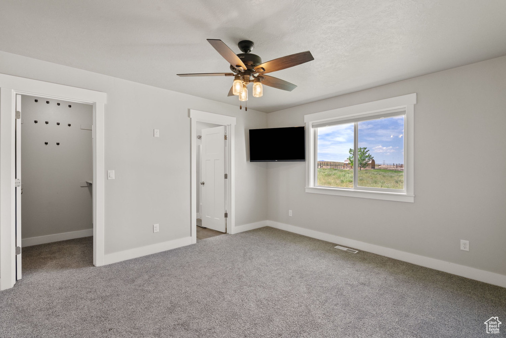 Unfurnished bedroom with a walk in closet, carpet floors, and a ceiling fan