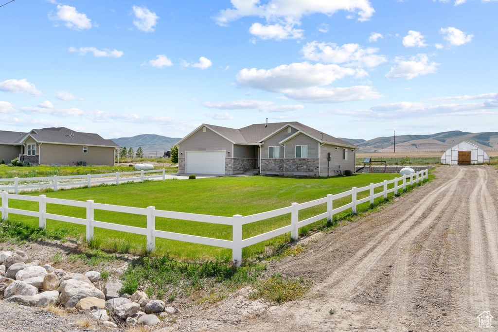 Single story home featuring dirt driveway, a mountain view, a garage, a rural view, and stone siding