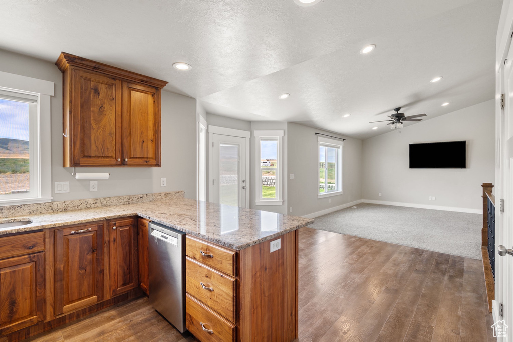 Kitchen with stainless steel dishwasher, a peninsula, brown cabinetry, wood finished floors, and vaulted ceiling