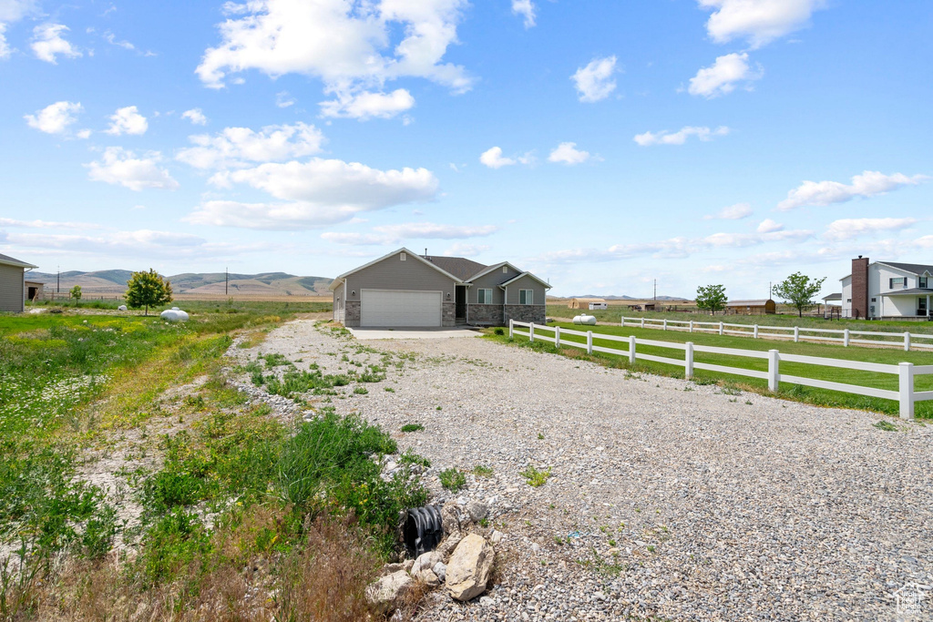 View of property exterior with gravel driveway, an attached garage, a view of countryside, and a mountain view