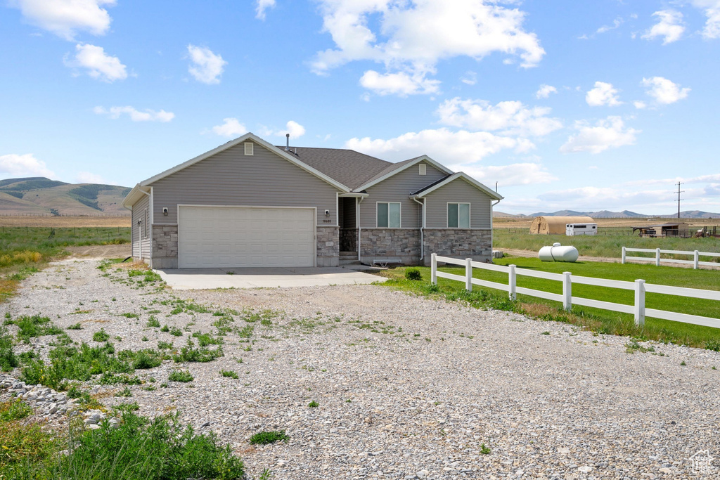 Single story home with dirt driveway, an attached garage, stone siding, and a mountain view