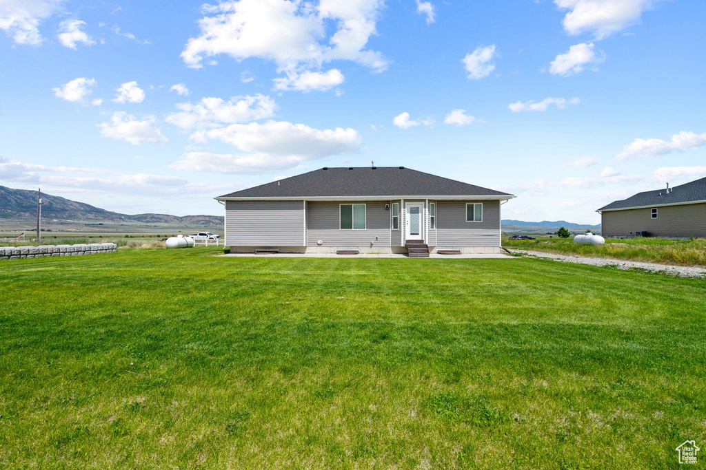 Back of house with entry steps, a patio, a mountain view, and a lawn