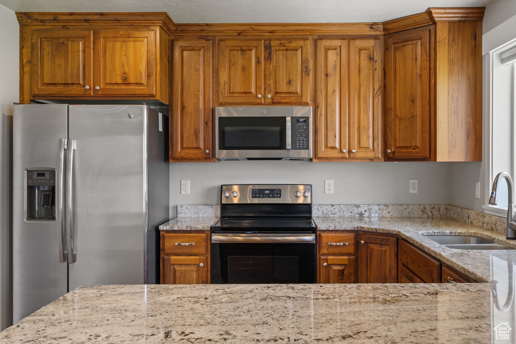 Kitchen featuring stainless steel appliances, brown cabinets, and light stone countertops
