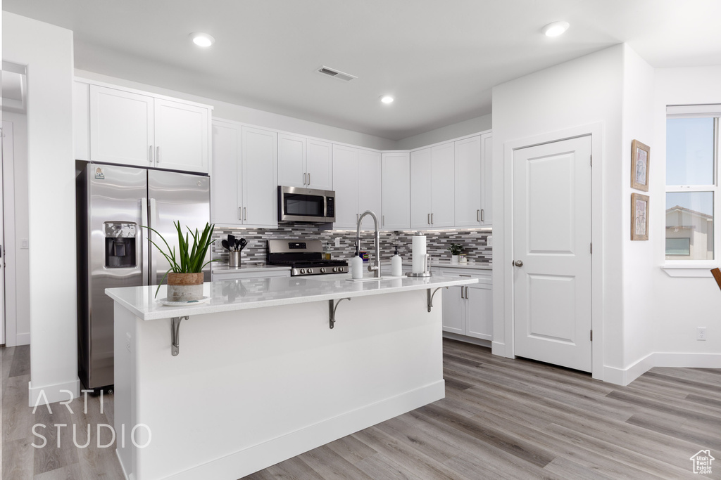 Kitchen featuring stainless steel appliances, a kitchen breakfast bar, light countertops, tasteful backsplash, and light wood finished floors