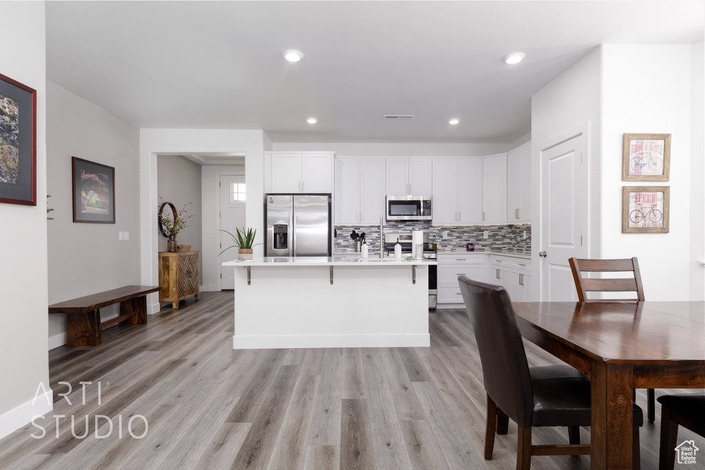Kitchen with appliances with stainless steel finishes, white cabinets, backsplash, light countertops, and a kitchen island with sink