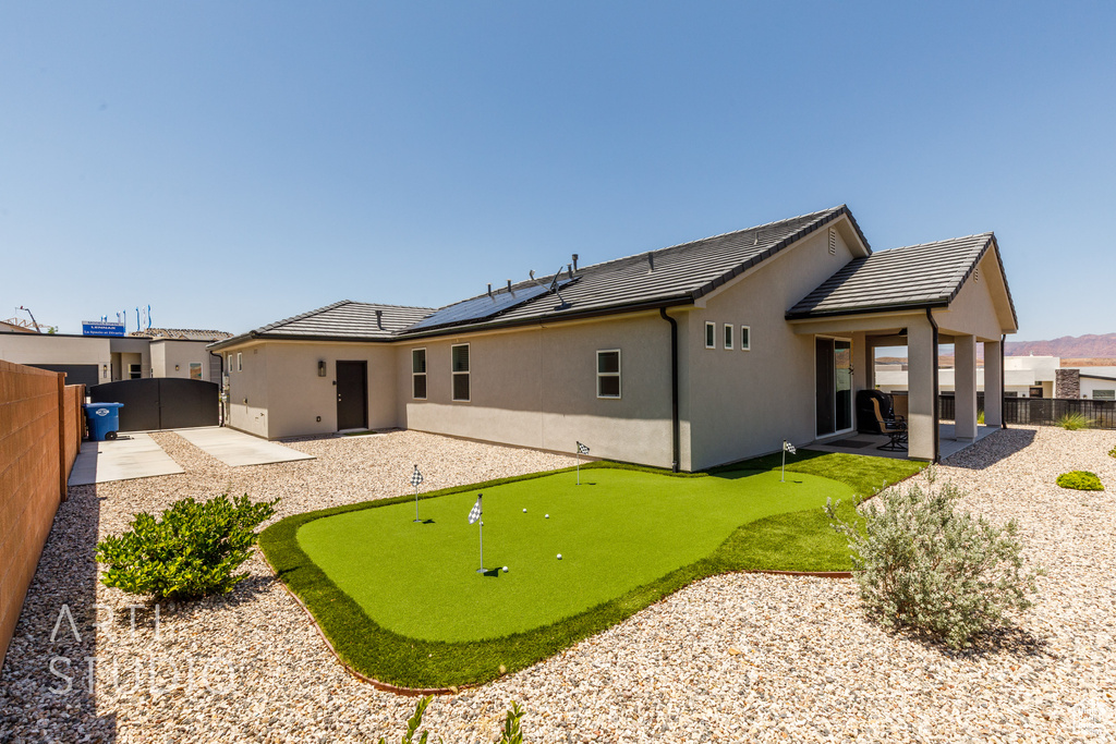Rear view of house with an area to practice putting, a patio, a fenced backyard, and stucco siding