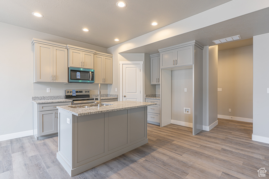Kitchen featuring appliances with stainless steel finishes, light wood finished floors, an island with sink, light stone counters, and recessed lighting
