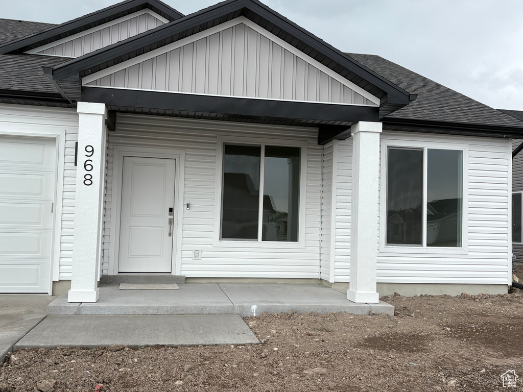 Property entrance featuring a garage, roof with shingles, and board and batten siding