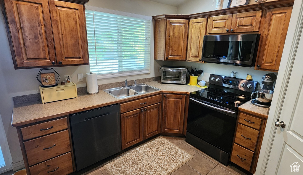 Kitchen with dishwasher, black / electric stove, a sink, and brown cabinetry