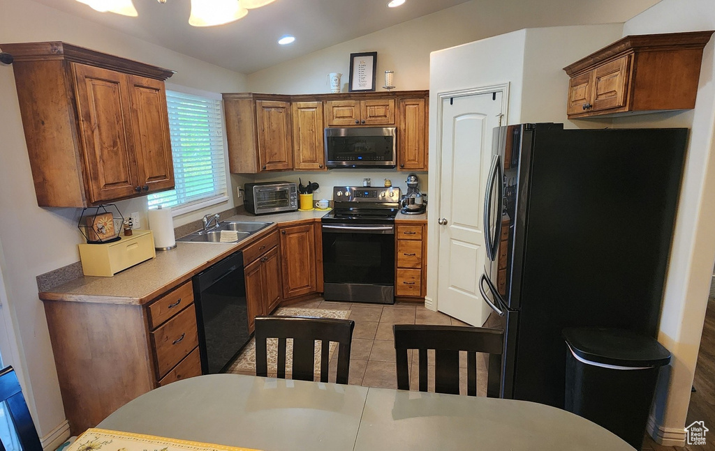 Kitchen featuring black appliances, a sink, brown cabinets, vaulted ceiling, and recessed lighting