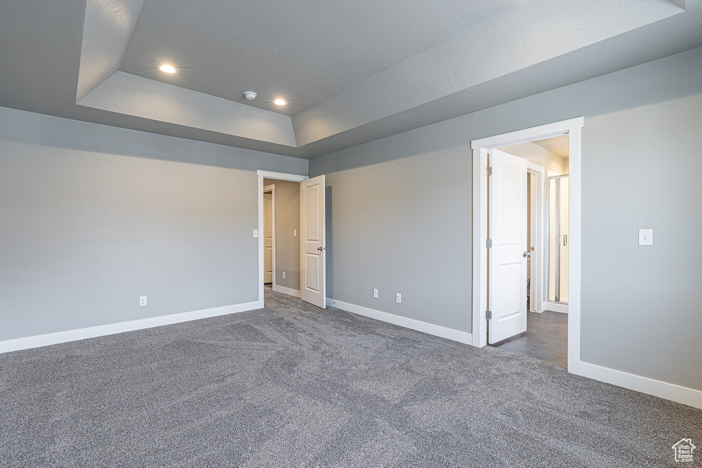 Unfurnished bedroom featuring a tray ceiling, dark carpet, and recessed lighting