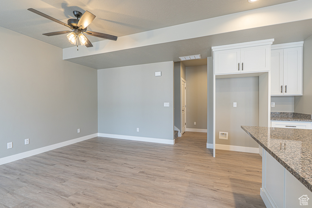 Kitchen with ceiling fan, white cabinets, light wood-style floors, stone counters, and open floor plan