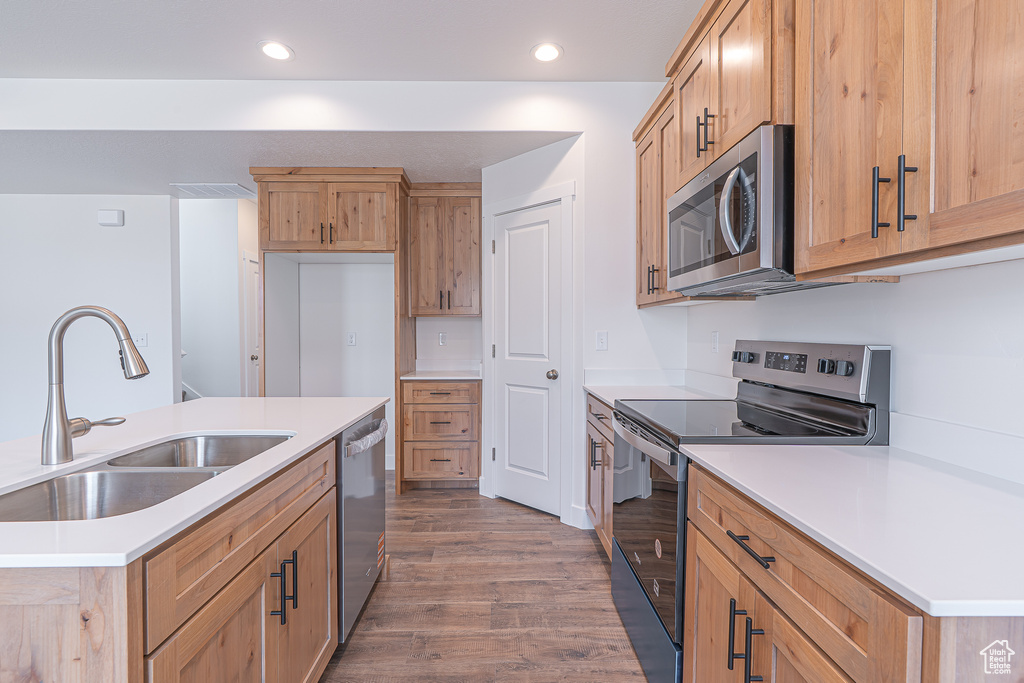 Kitchen with appliances with stainless steel finishes, wood finished floors, recessed lighting, light countertops, and a kitchen island with sink