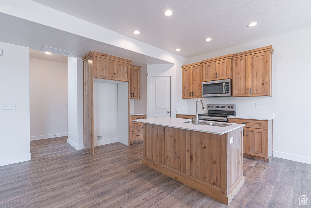 Kitchen featuring stainless steel appliances, light countertops, recessed lighting, wood finished floors, and a center island with sink