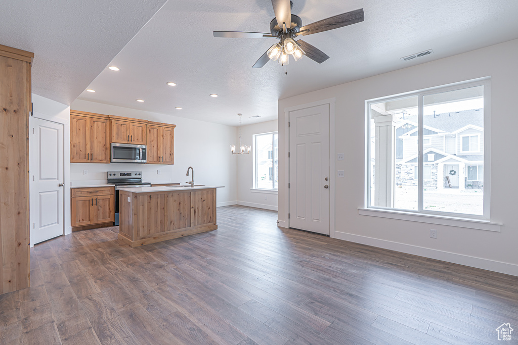 Kitchen with appliances with stainless steel finishes, recessed lighting, a kitchen island with sink, a chandelier, and dark wood-style flooring