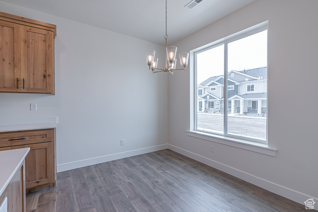 Unfurnished dining area with healthy amount of natural light, a chandelier, and wood finished floors