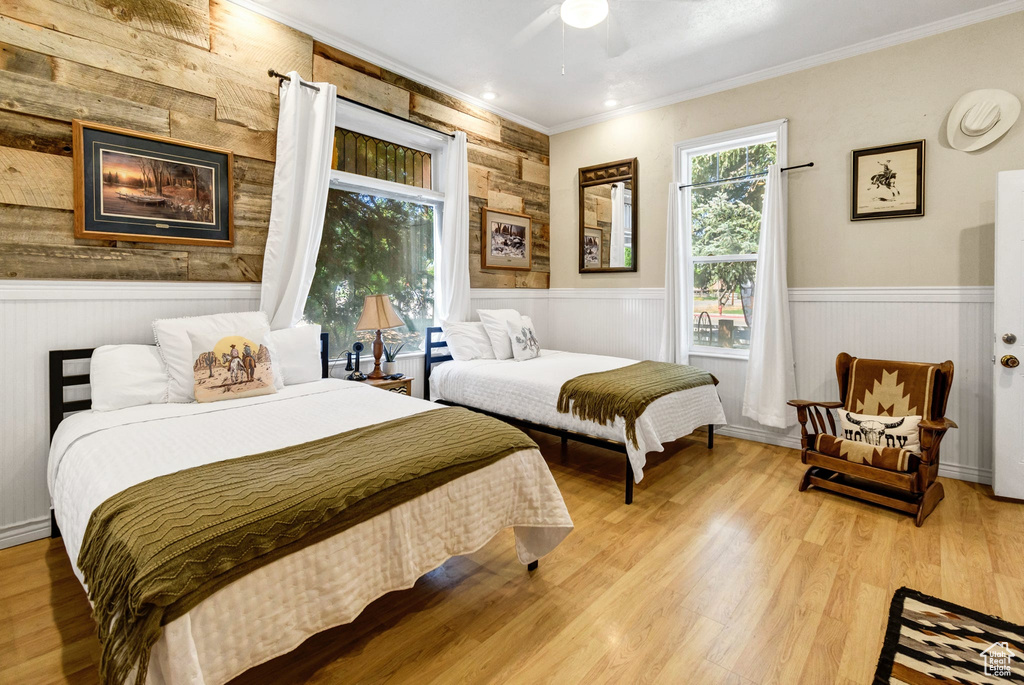 Bedroom with wainscoting, ornamental molding, wood finished floors, wood walls, and ceiling fan