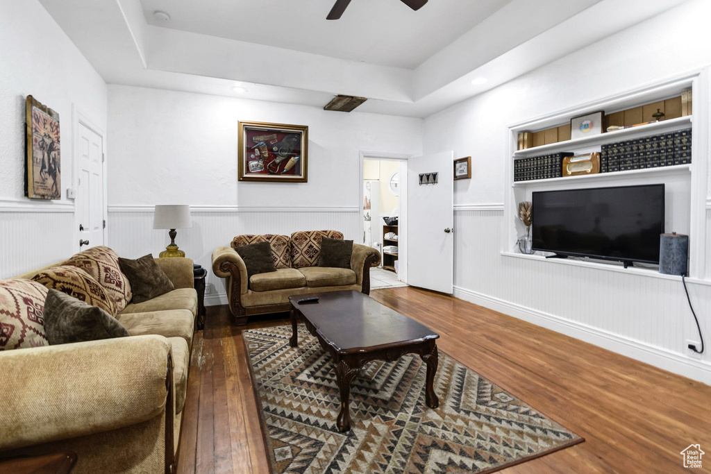 Living area with wood finished floors, a ceiling fan, a tray ceiling, recessed lighting, and a wainscoted wall