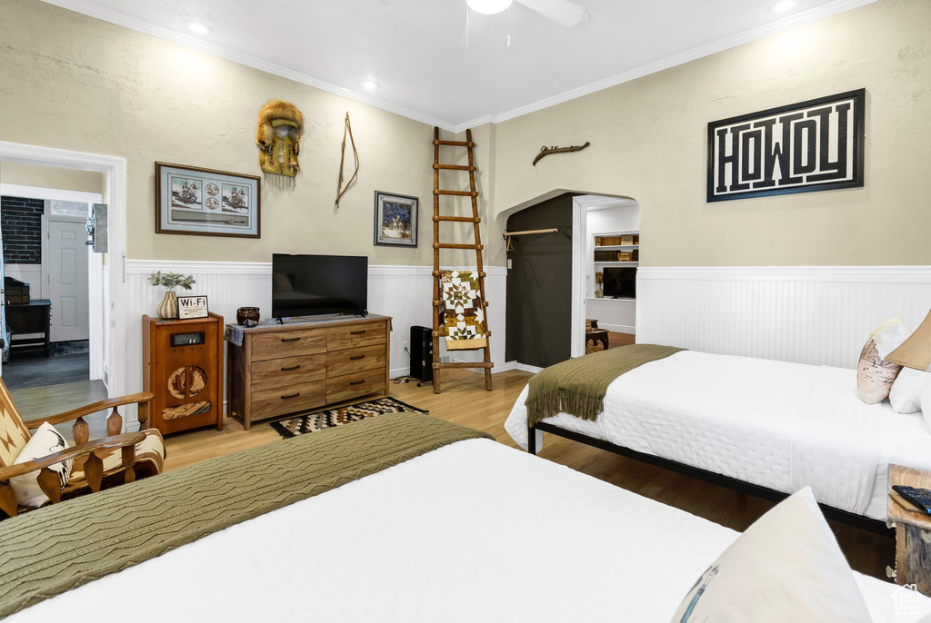 Bedroom with a wainscoted wall, wood finished floors, ornamental molding, arched walkways, and recessed lighting