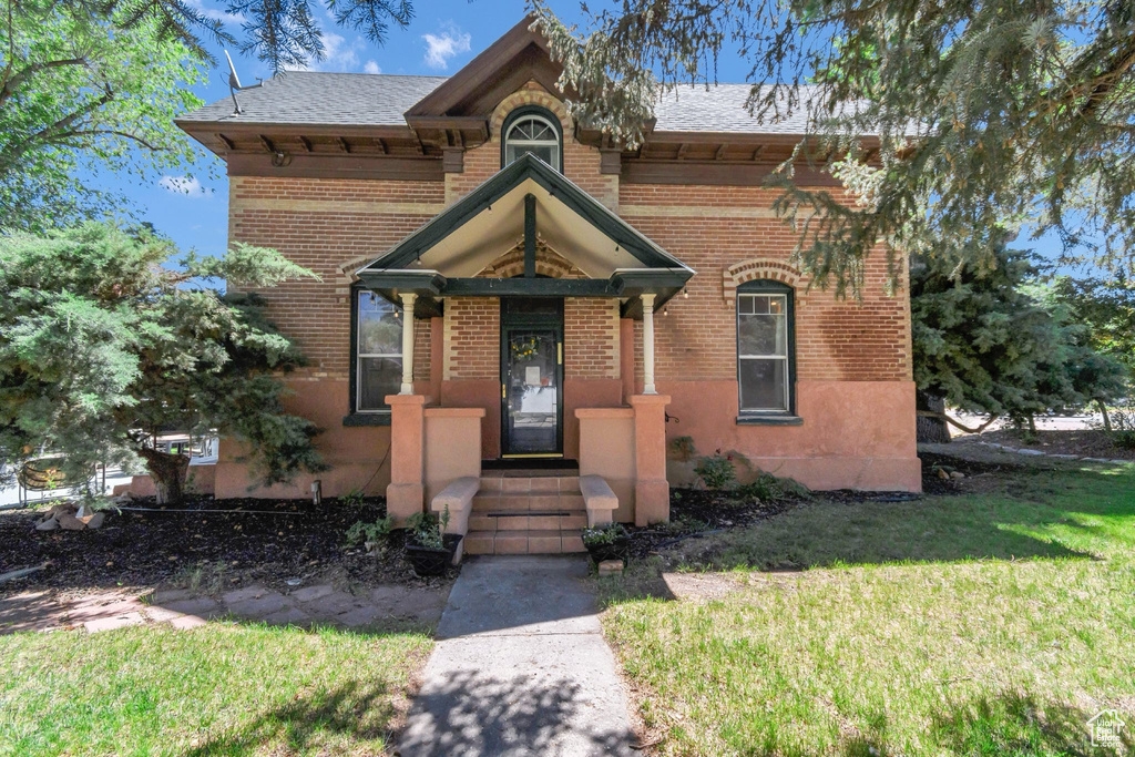 View of front facade featuring brick siding, a front yard, and a shingled roof