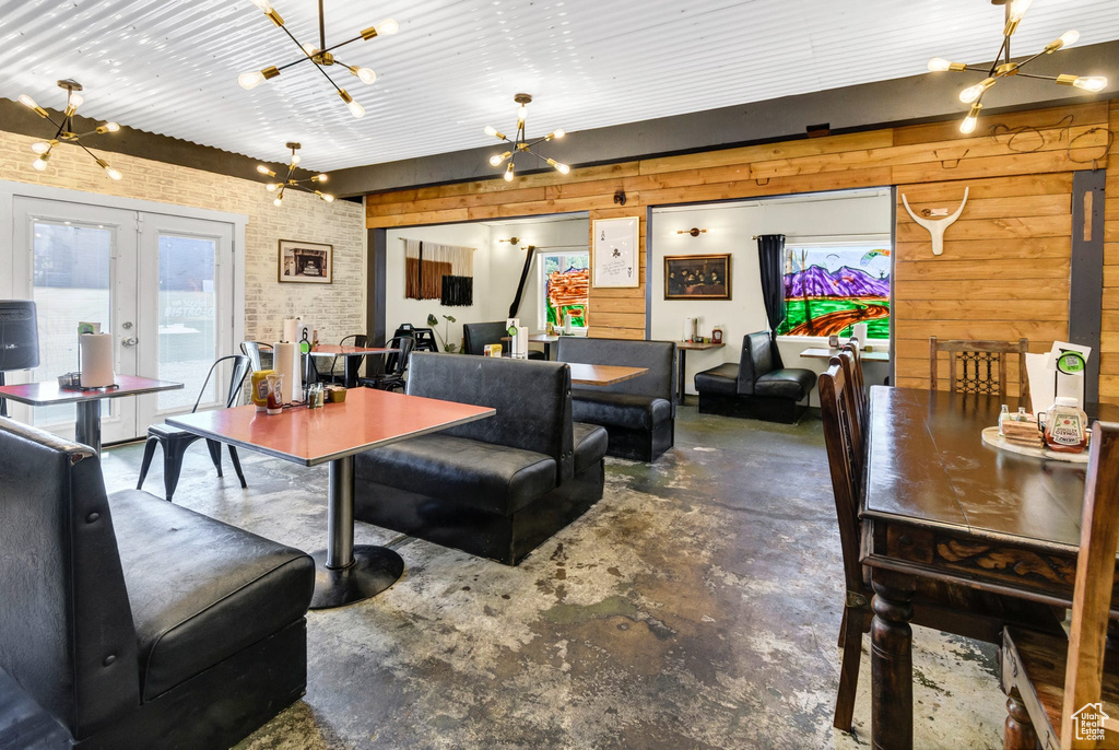Dining area featuring a chandelier, finished concrete floors, french doors, and wood walls