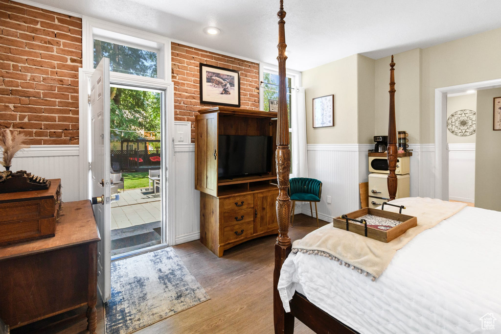 Bedroom featuring access to outside, wood finished floors, a wainscoted wall, and brick wall