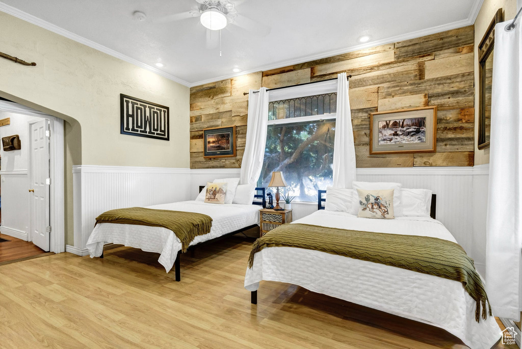 Bedroom with ornamental molding, wood finished floors, a wainscoted wall, wooden walls, and a ceiling fan